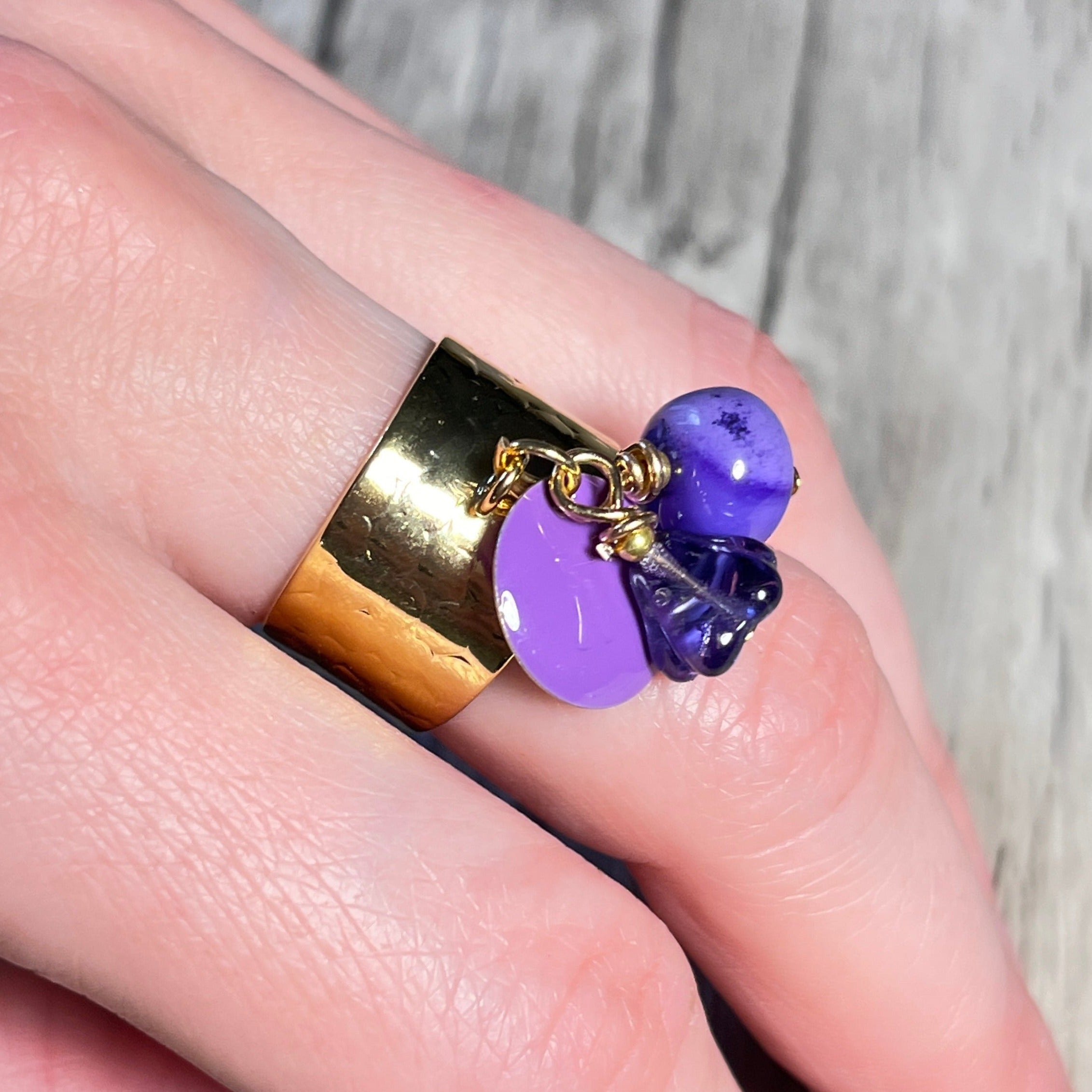 maint portant une bague dorée pierre naturelle opale violette et sequin emaille